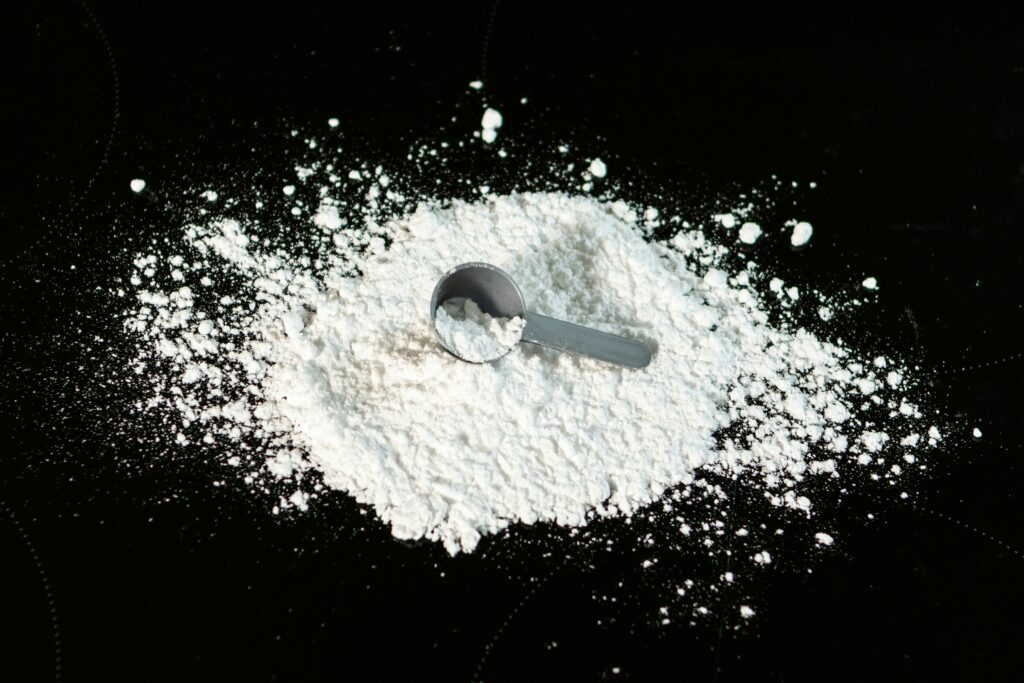 Creatine monohydrate powder with measuring scoop on a dark background